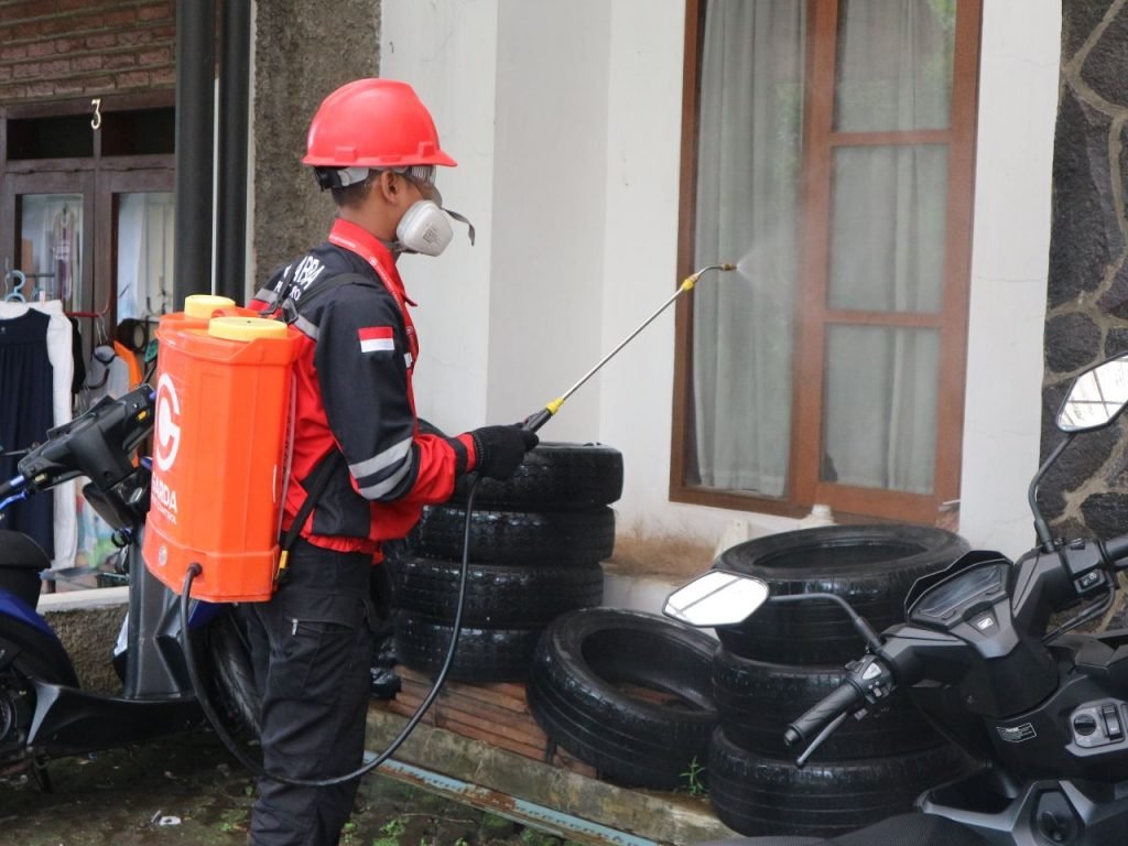 A worker in safety gear sprays disinfectant outside a building, ensuring cleanliness.